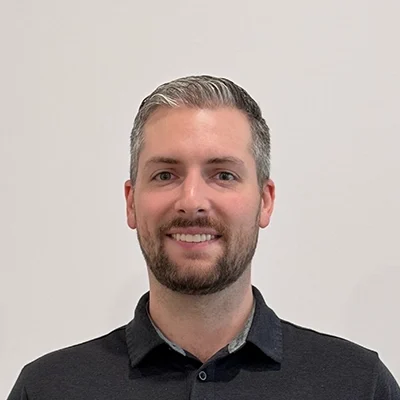 Chiropractor Benjamin Hartman Smiling In Front Of White Wall